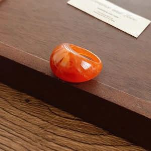 Détail macro d'une bague bombée en résine orange marbrée sur un coffret en bois