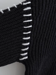 Dettaglio macro delle cuciture a contrasto bianche sulla spalla di un maglione nero