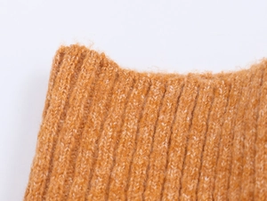 Dettaglio macro della trama in maglia giallo zenzero e del polsino a coste del maglione
