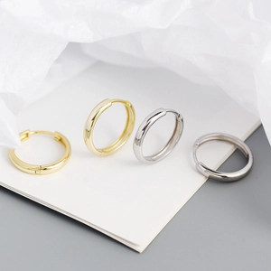 Detailed view of polished gold and silver s925 hoop earrings on a textured background