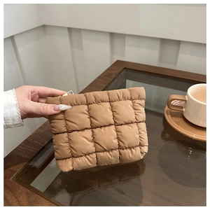 Detail of khaki quilted puffer handbag with padded checkered texture held by hand