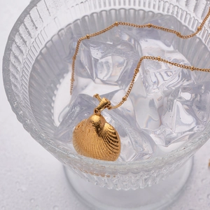 Golden scallop shell pendant necklace placed in a glass bowl with ice cubes
