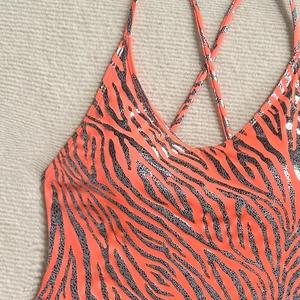 Detail of metallic silver zebra print on orange swimsuit with thin cross-back straps