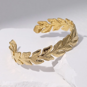 Adjustable golden stainless steel leaf open bangle placed on a white stone surface