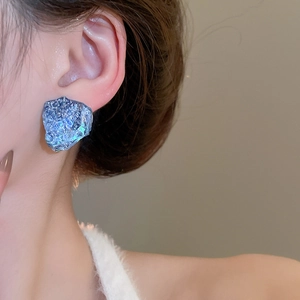 Close-up of blue irregular resin stud earrings with crystal texture on model's ear