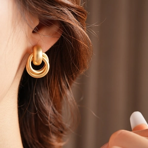 Close-up of golden matte double-hoop earrings featuring a brushed metal geometric design