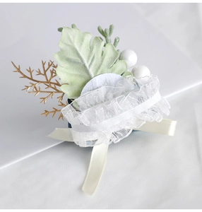 Detail of white lace wedding corsage with green velvet leaf and elegant satin ribbon
