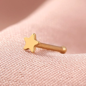 Macro view of a gold star-shaped stainless steel nose stud on soft pink fabric