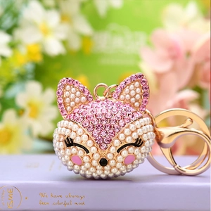 Macro detail of fox head keychain featuring pink rhinestones and white pearls on gold metal