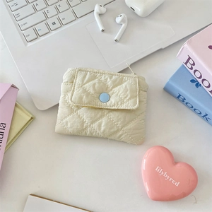 Quilted beige coin purse with blue snap button next to a laptop and headphones