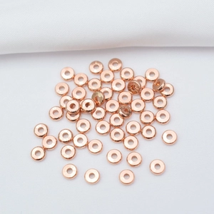 Flat rose gold spacer beads in disc shape for DIY jewelry making on white fabric