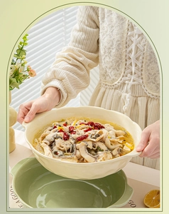 Detail of a large cream ceramic soup bowl with scalloped edges being held with food