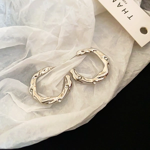 Macro view of C-shaped silver earrings with twisted lava texture and inlaid zircons