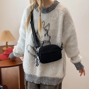 Detail of a small black nylon crossbody bag paired with a gray knit sweater