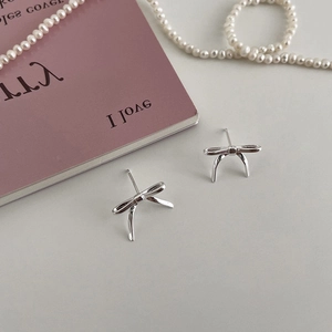 Detail view of silver bow earrings with pearl necklace on a white elegant background