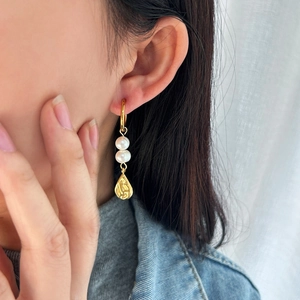 Dettaglio di modella che indossa orecchini d'oro con perle naturali e pendenti a goccia