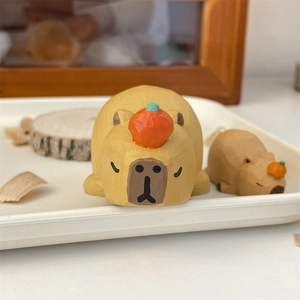 Macro view of hand-carved wooden capybara figurines with orange accents on a white tray