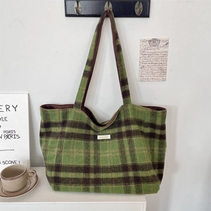 Detail of green plaid wool tote bag featuring a stitched logo label and long shoulder strap