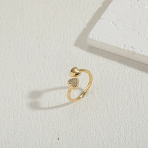 Macro detail of adjustable gold double heart ring with clear zircon stones on white surface
