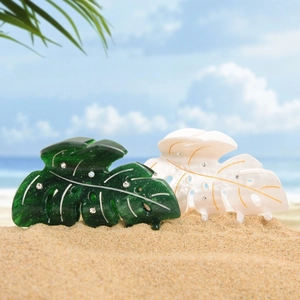 Leaf-shaped acetate hair clips with rhinestones and marble texture on summer beach background