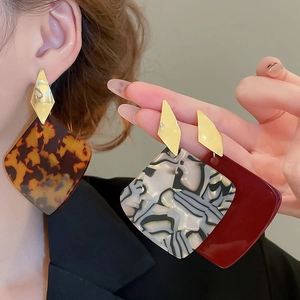 Close-up of geometric acrylic earrings with tortoise and marble patterns on gold studs