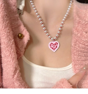 Detailed view of pearl necklace with a pink heart pendant and That's All Right text