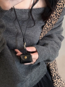 Detail shot of a black leather mini neck pouch with metal button on a grey sweater