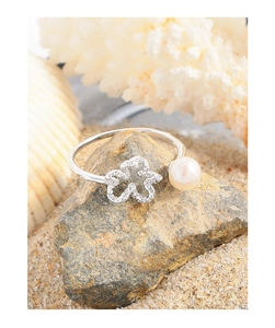 Close-up of S925 silver flower ring with pearl on a rock with seaside background