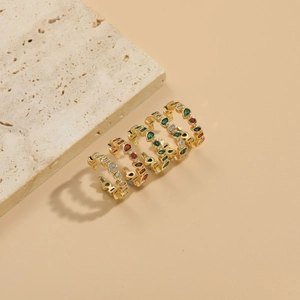 Detailed top view of five gold-plated rings with colorful zircons on a beige stone surface