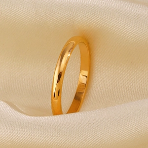 Minimalist gold stainless steel band ring displayed on smooth beige silk background