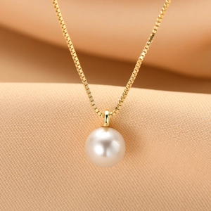Macro shot of a round white freshwater pearl pendant on a gold box chain over silk
