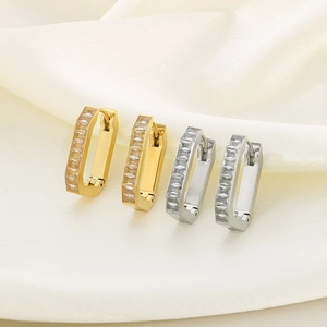 Close-up of gold and silver U-shaped earrings with rectangular cubic zirconia on white silk