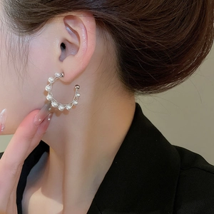 Close-up of elegant C-shaped silver earrings with white pearls worn by a model
