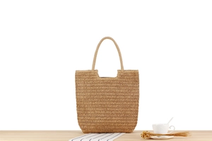Detailed close-up of a hand-woven straw shoulder bag on a light wood grain surface