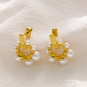 Macro shot of gold hoop earrings with white baroque pearls on white fabric background
