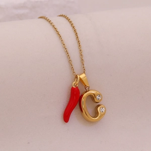 Macro view of gold chili and crystal-inlaid letter C pendants on a stainless steel necklace
