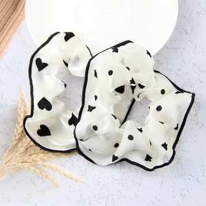 Detail of white mesh scrunchies featuring black heart and polka dot patterns with piping