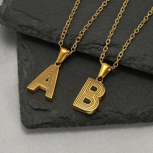 Detail of gold initial necklaces A and B with striped texture on a dark stone slab