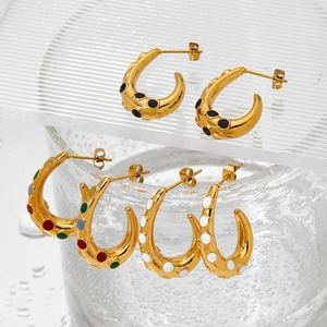 Three pairs of gold C-shaped hoop earrings with colorful enamel dots on a glass background