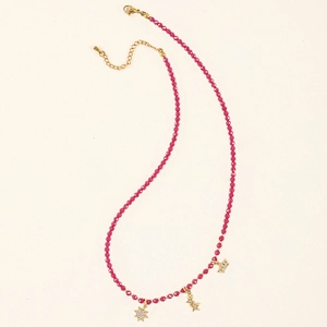 Detail of beaded necklace with pink stones, star and crown zircon pendants on cream background
