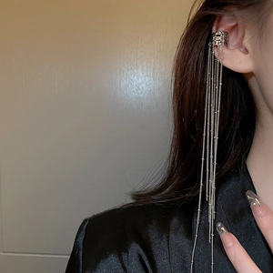 Detail of silver irregular C-shaped ear cuff with long metallic fringe tassels on ear
