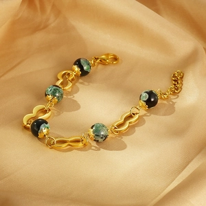 Détail d'un bracelet en acier doré 18K avec perles en résine vert et noir sur soie dorée