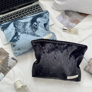 Detailed view of crushed velvet makeup bags in marble blue and black on white bedding