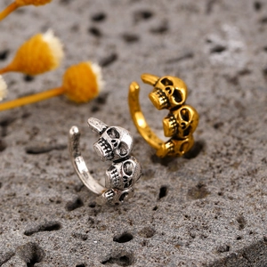 Detailed close-up of vintage silver and gold skull ear cuffs on a textured rock surface