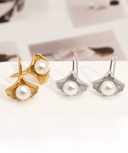 Close-up of gold and silver ginkgo leaf earrings with white pearls on a stone surface