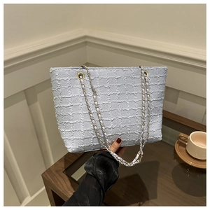 Close-up of light blue tweed tote bag with gold chain strap held by a model