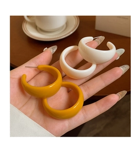 Detail of C-shaped acrylic earrings in white and yellow held by a hand in a lifestyle setting