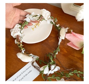 Macro detail of white artificial flower crown with green leaves and woven rattan vines