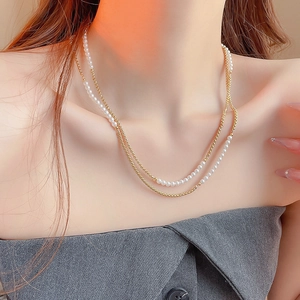 Gros plan d'un collier double épaisseur avec billes dorées et perles blanches sur modèle