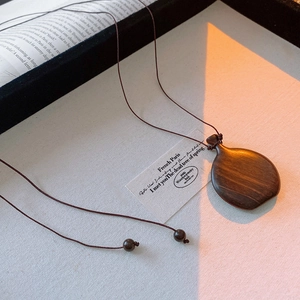 Macro detail of teardrop wooden pendant necklace on book with warm natural sunlight